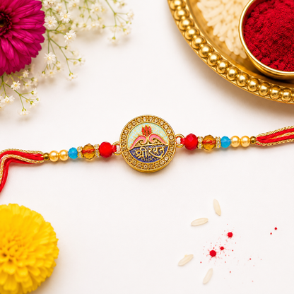 A traditional Indian Rakhi bracelet with a gold-toned circular charm featuring Devanagari text, decorated with red, blue, and gold beads, laid out on a white surface with festive props including a yellow flower, white baby's breath, and a gold plate with red powder.