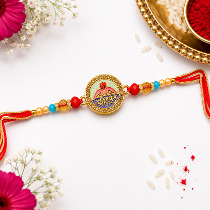 A traditional Indian Rakhi with a gold circular charm featuring a colorful Lakshmi design and Devanagari text, decorated with red and blue beads, gold spacer beads, and red tassels, laid out on a white surface with festive props.